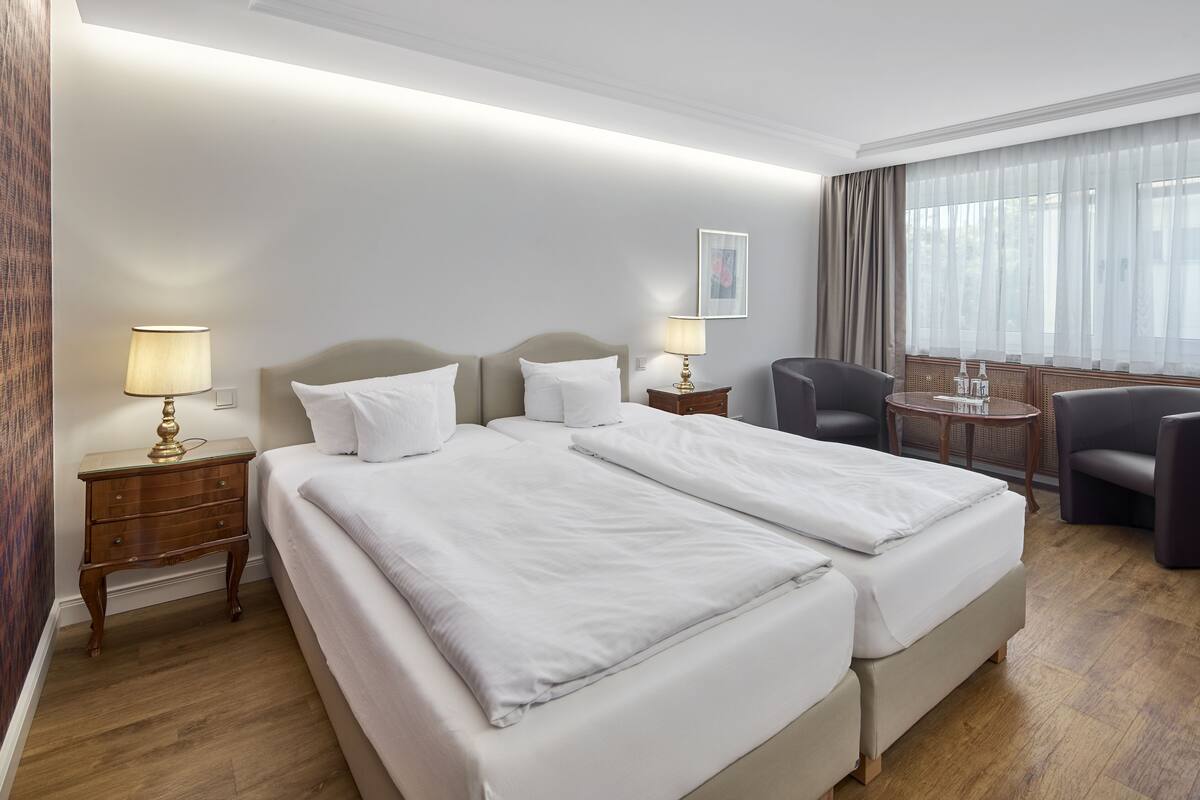 A hotel room with two beds, a desk, a chair, and a window with curtains.