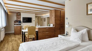 Habitación de hotel con techo de madera, una cama con ropa blanca, un escritorio con silla, un armario y un televisor en la pared.