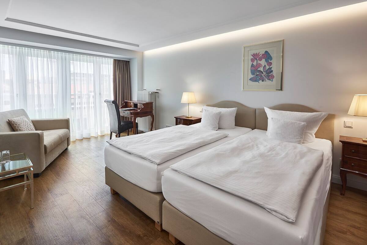 A hotel room with two beds, a desk, a chair, and a sofa.