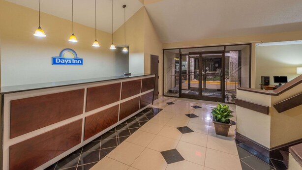 A reception area with a Days Inn sign, a reception desk, a potted plant, and a staircase. - Days Inn by Wyndham Yadkinville (Yadkinville)