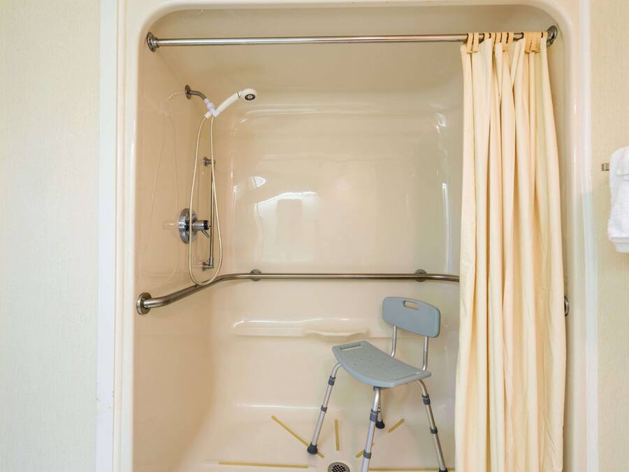 A shower area with a grab bar, a shower chair, and a curtain.