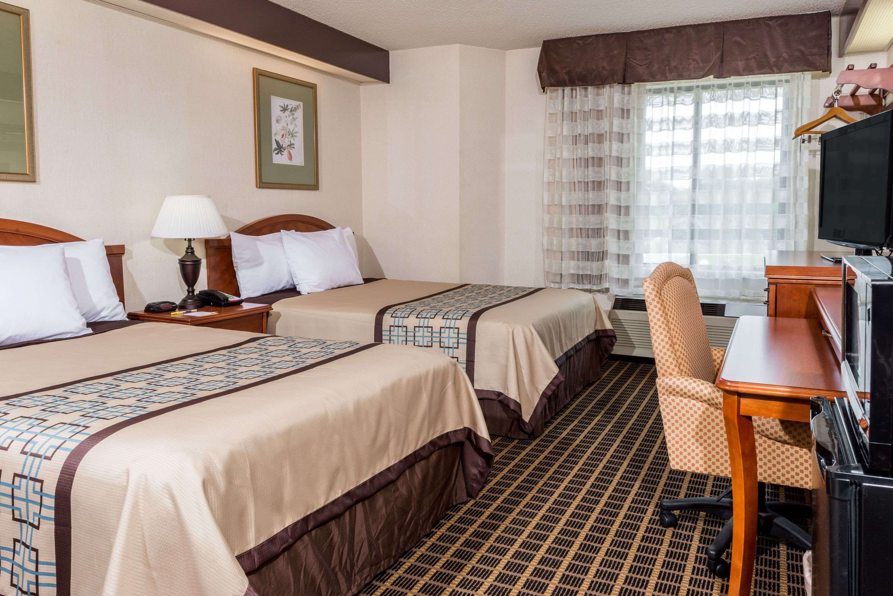 Une chambre d’hôtel avec deux lits, un bureau, une chaise, une télévision et une fenêtre avec des rideaux.