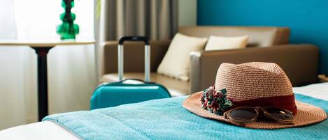 A hotel room with a bed, a suitcase, a hat, sunglasses, and a table with a vase of flowers.