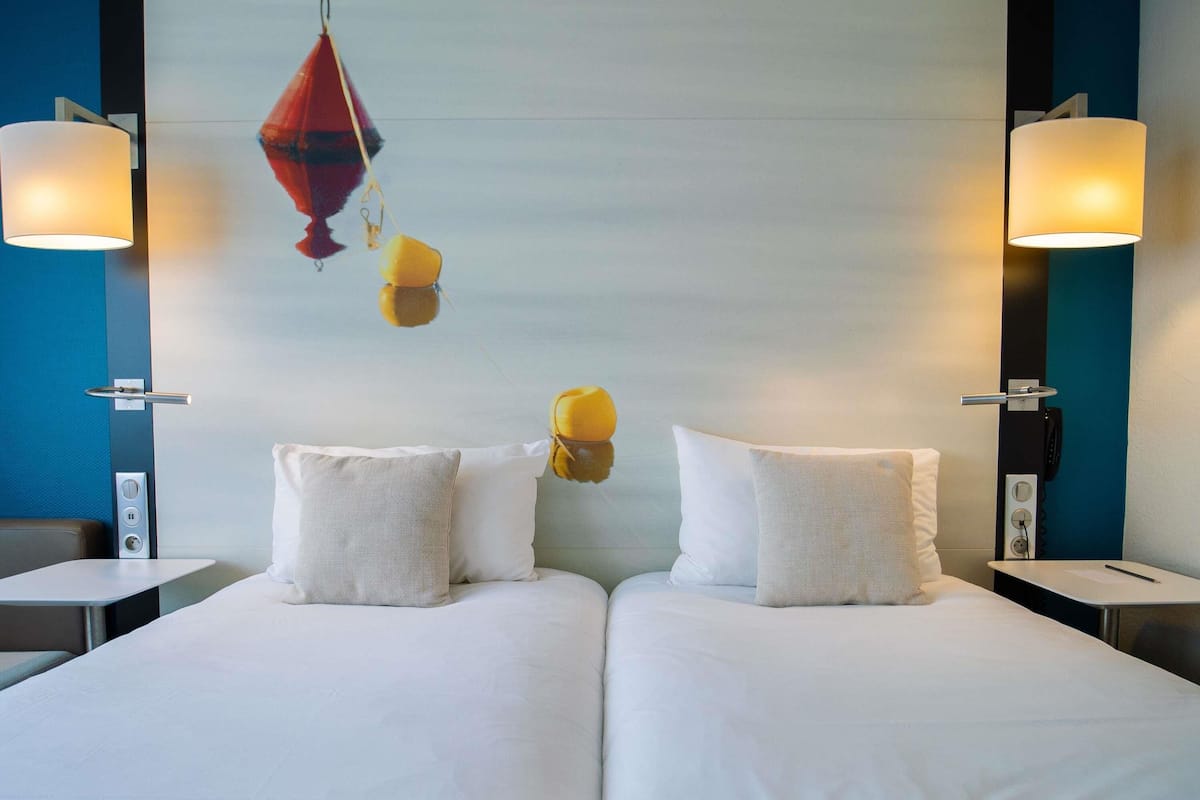 A double bed with white linens, two bedside tables, and wall-mounted lamps.