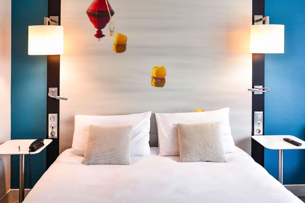 A hotel room with a bed, two bedside tables, a telephone, and a wall-mounted lamp.