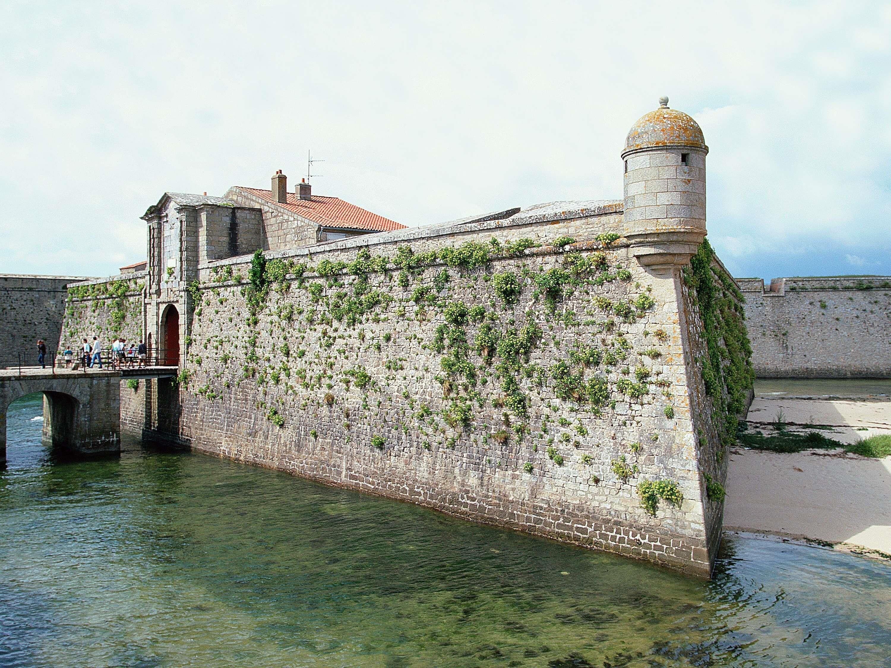 A stone wall with a bridge and a tower, surrounded by water.
