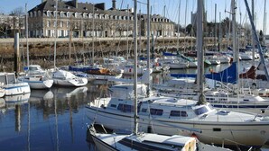 A marina with multiple boats docked, a large building in the background, and a clear sky. - Mercure Lorient Centre Hotel (Lorient)