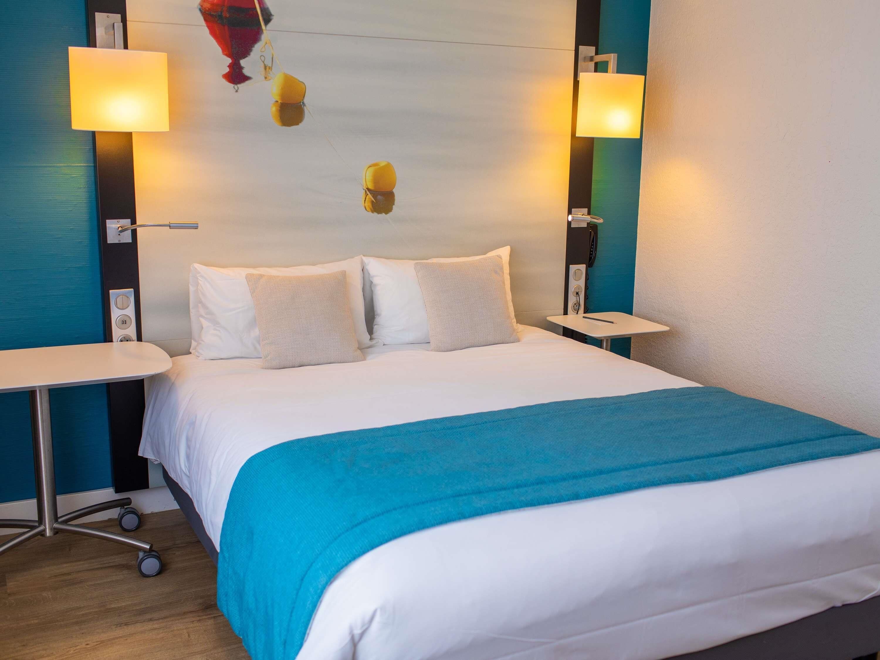 A hotel room with a bed, two bedside tables, and two wall-mounted lamps.