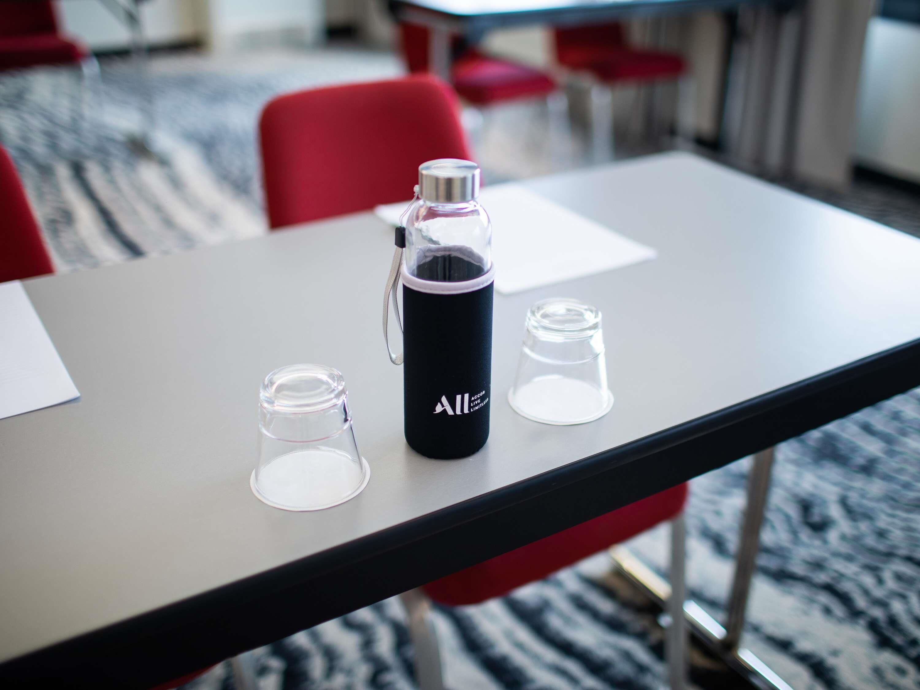 Una mesa con una botella de agua negra y dos vasos transparentes.
