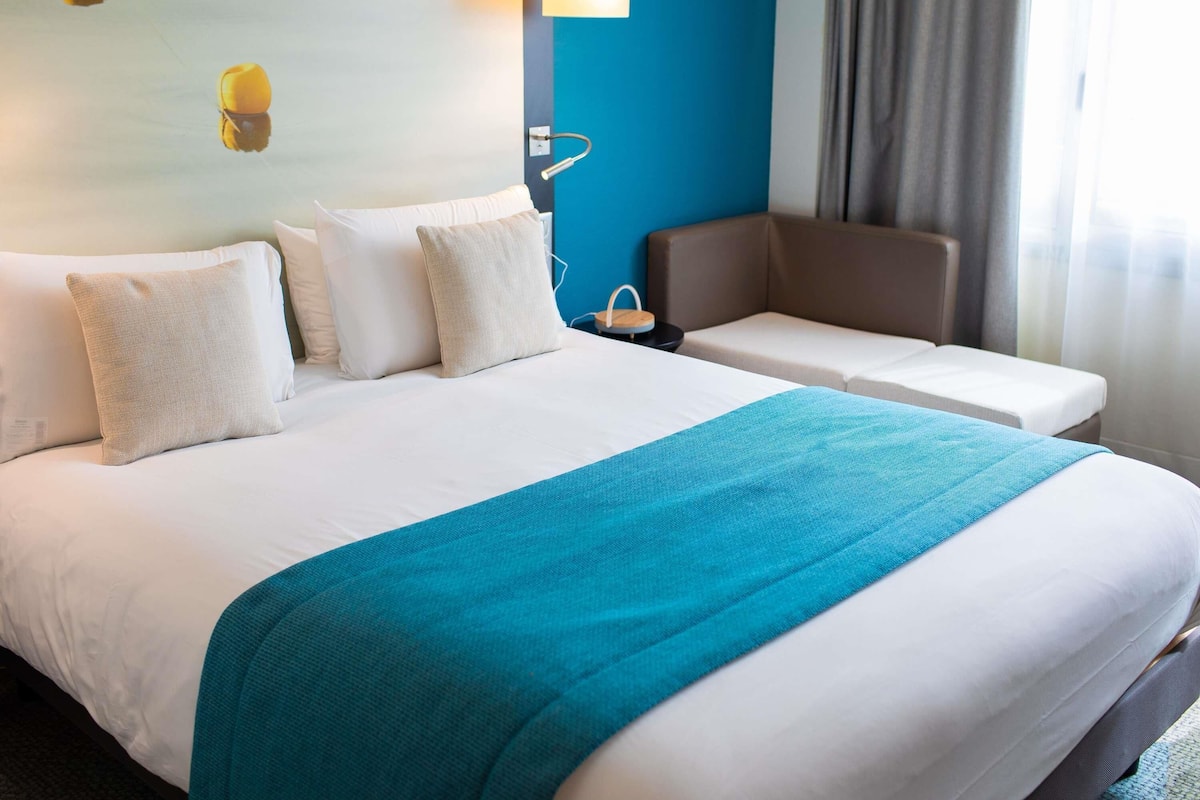 A hotel room with a large bed, a seating area, and a wall-mounted lamp.