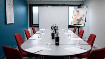 A conference room with a long table, red chairs, water bottles, and a projector screen.