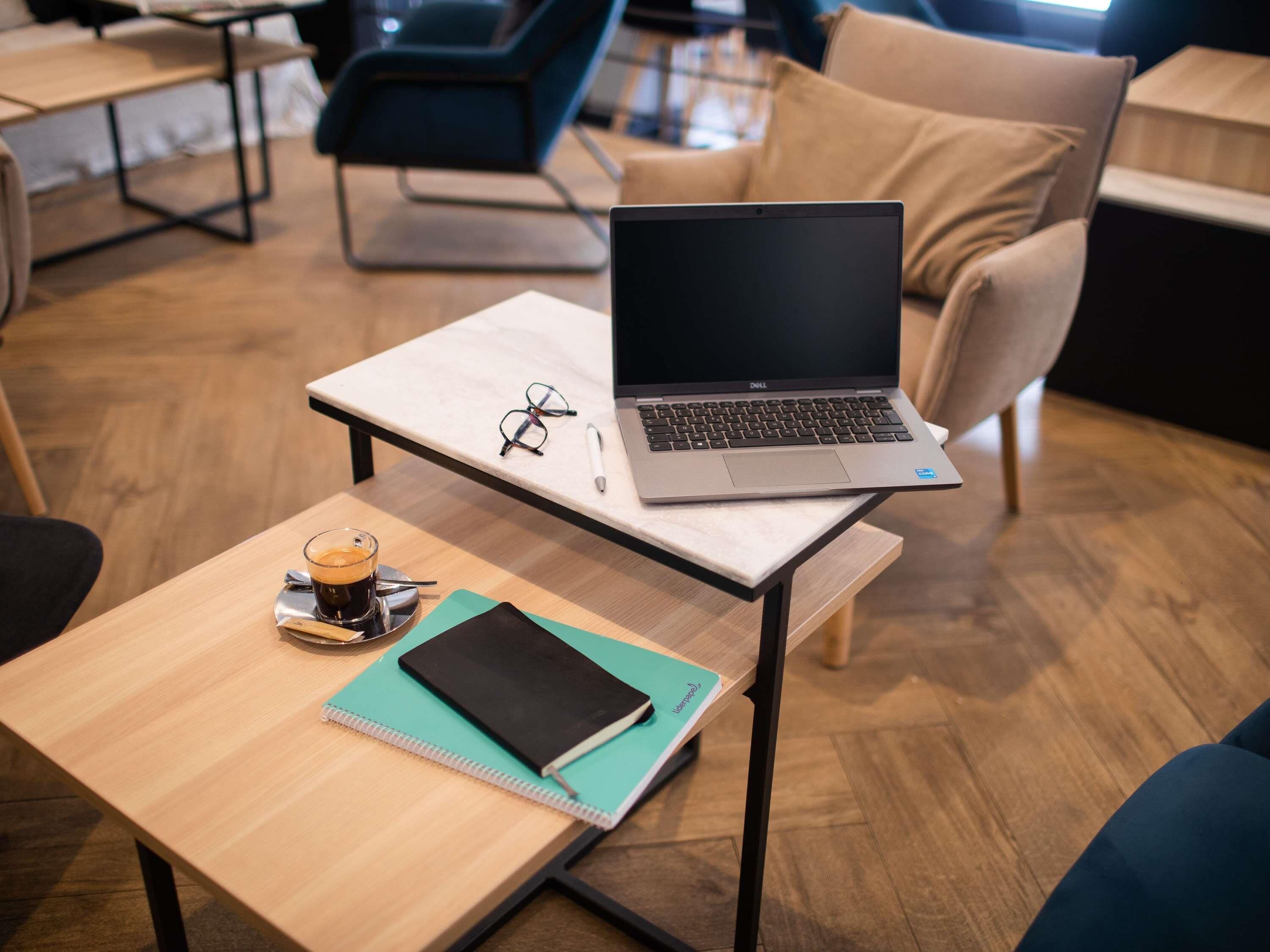 Ein Laptop auf einem Tisch, zusammen mit einem Notizbuch, einer Brille und einer Kaffeetasse.