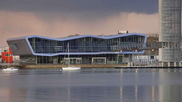 A modern building with a unique wavy roof design, situated by a body of water with boats. - Mercure Lorient Centre Hotel (Lorient)