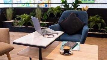 A modern indoor space with a laptop on a table, a chair with a cushion, a coffee cup on a small table, and potted plants in the background.