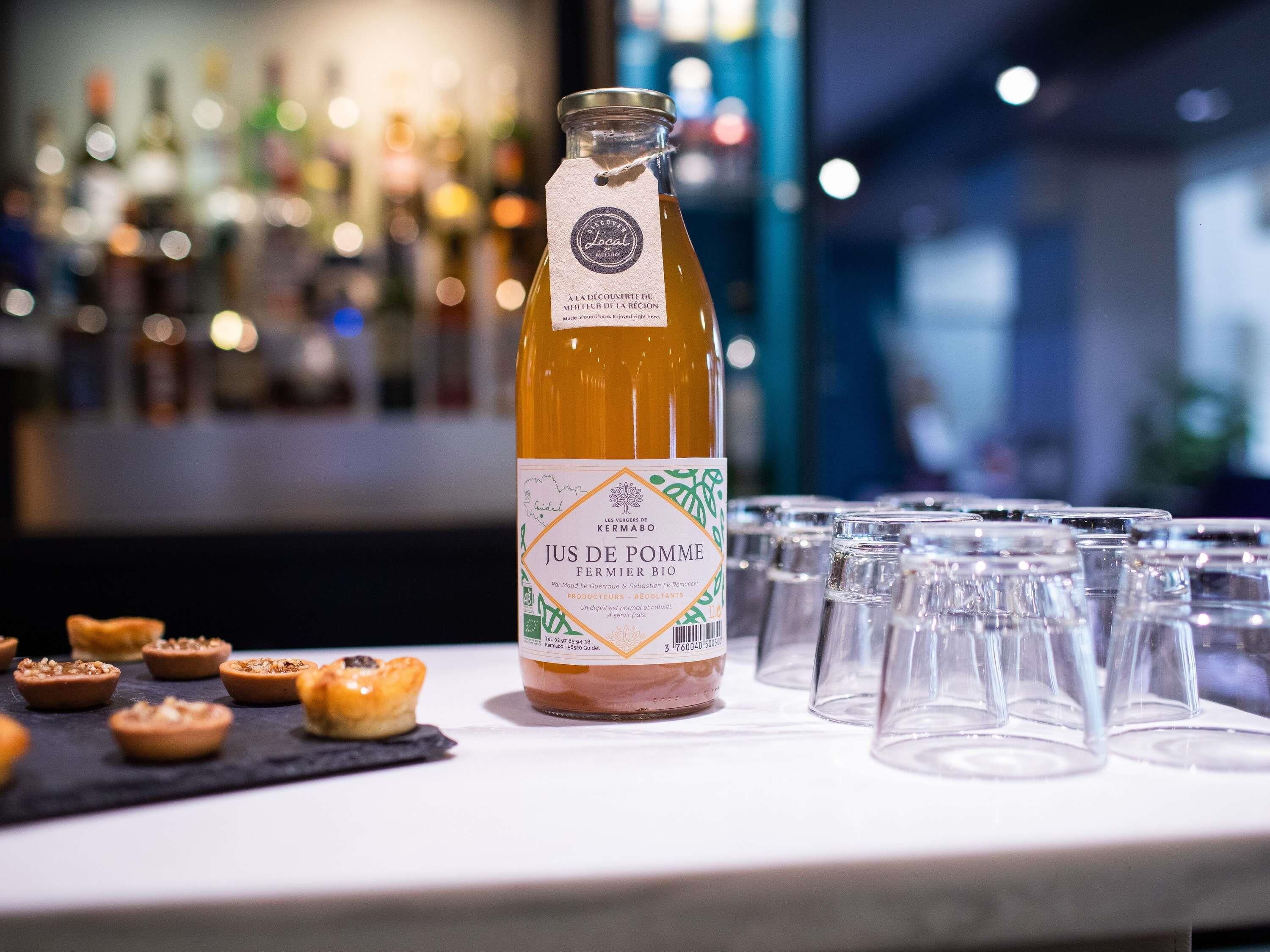 A bottle of Jus de Pomme Fermiere on a bar counter with glasses and pastries.