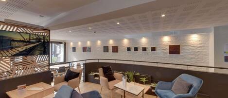 A modern lounge area with seating, a view of a bridge, and a white brick wall with artwork.