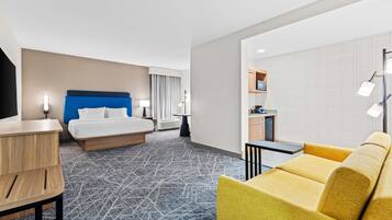 A hotel room with a bed, a desk, a sofa, a kitchenette, and a patterned carpet.