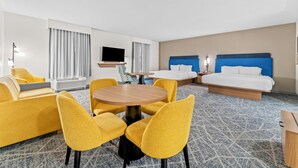 A hotel room with a sofa, two single beds, a TV, a round table, and a patterned carpet.
