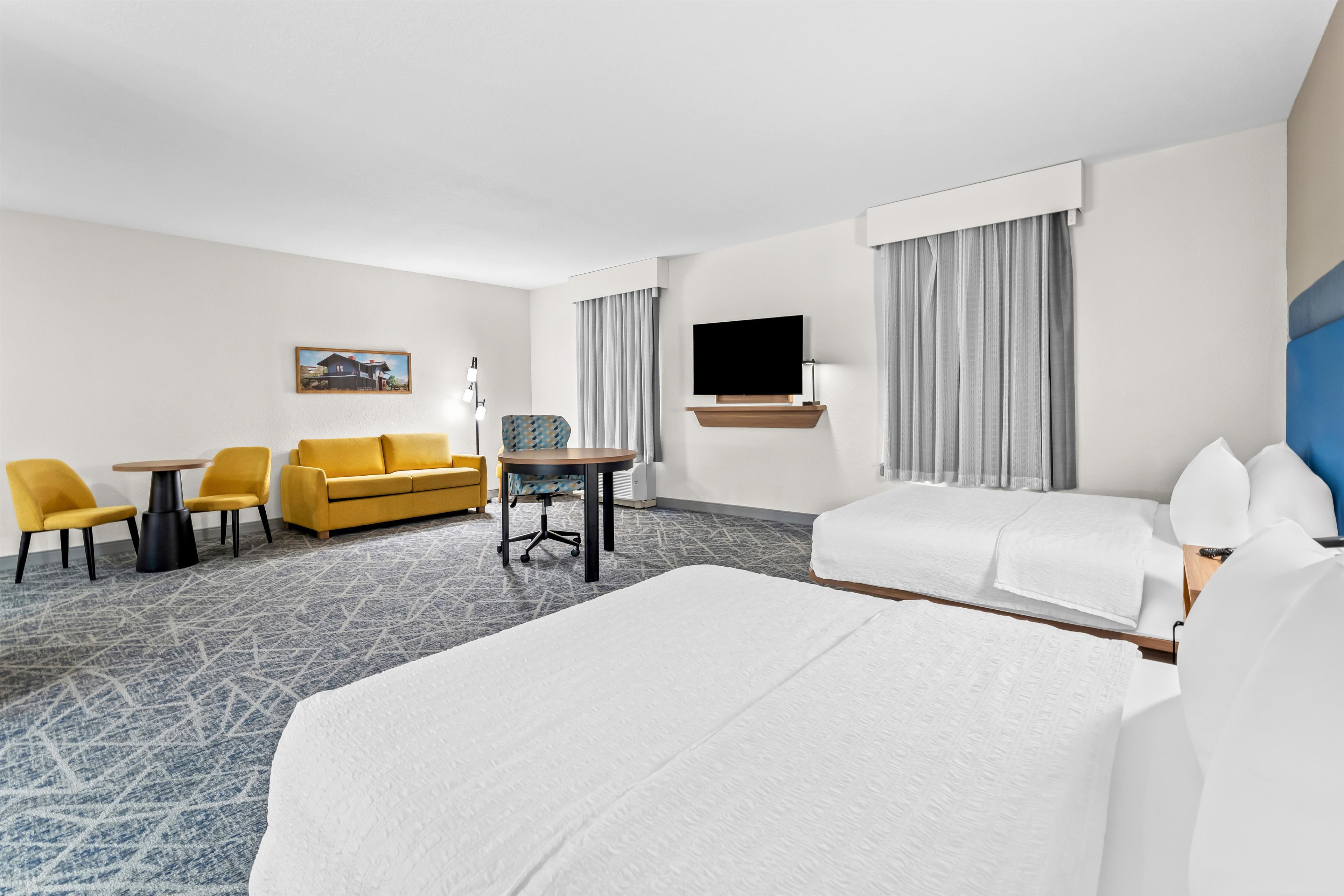 Une chambre d’hôtel comprenant un lit, un canapé, un bureau avec des chaises, une télévision et un tableau au mur.