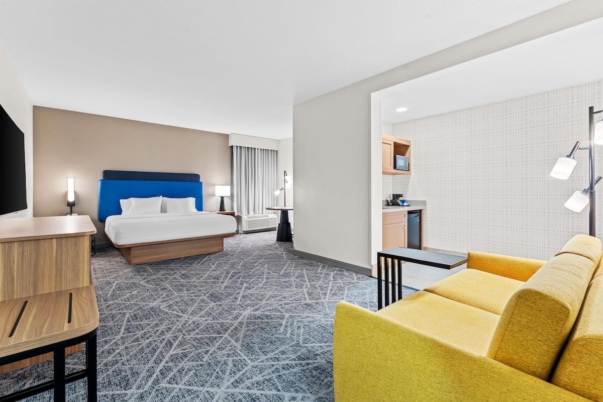 Ein Hotelzimmer mit einem Bett, einem Schreibtisch, einem gelben Sofa, einer Küchenzeile und einem Badezimmer.