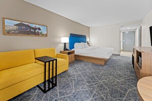 Una habitación de hotel con una cama, un sofá amarillo, una mesita de noche, una lámpara y un cuadro en la pared.