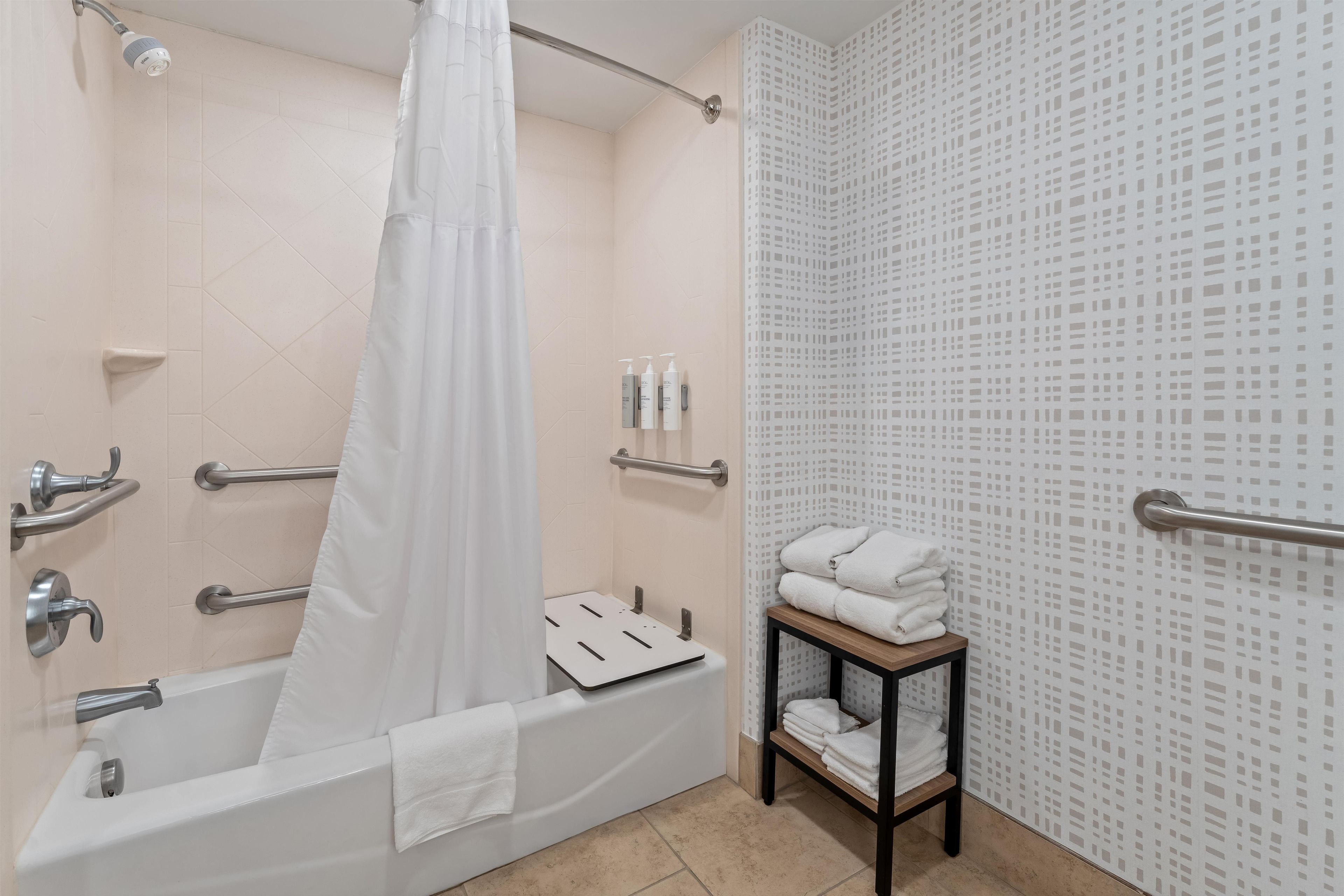 Une salle de bain moderne équipée d’une baignoire, d’un rideau de douche, d’un porte-serviettes et d’une étagère pour les articles de toilette.