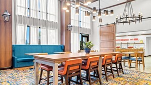 A modern dining area with a long wooden table, blue sofa, and orange chairs. - Hampton Inn & Suites Tifton (Tifton)