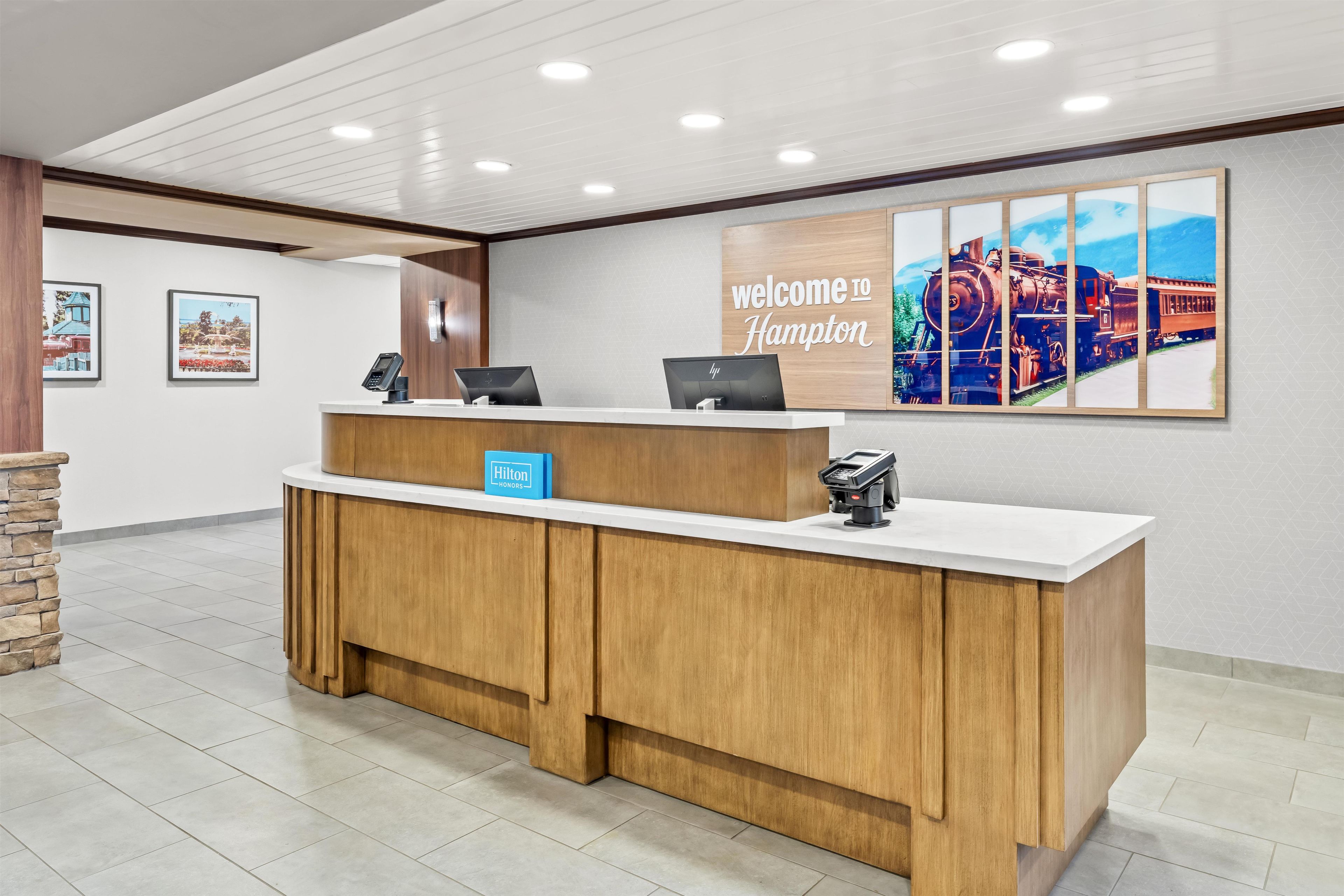 Un comptoir d’accueil d’hôtel avec une pancarte « Bienvenue à Hampton », une autre indiquant « Hilton Honors » et le logo « Hilton ».