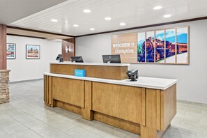 Una recepción de hotel con un cartel que dice 'Welcome to Hampton', un cartel de 'Hilton Honors' y el logotipo de 'Hilton'.