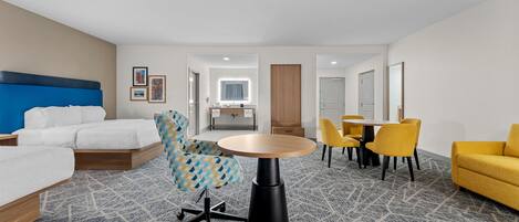 A hotel room with a bed, a desk, a chair, a dining table with chairs, and a bathroom visible through an open door.