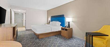 A hotel room with a bed, bedside table, lamp, chair, and a desk.