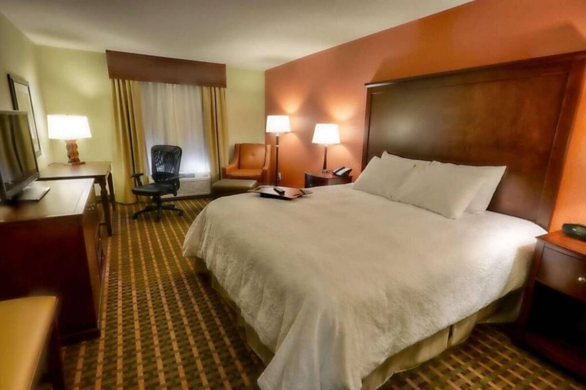 Ein Hotelzimmer mit Bett, Schreibtisch, Stuhl, Lampen und einem Fernseher.