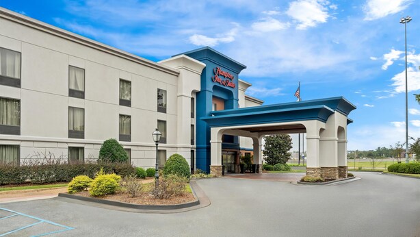 A hotel entrance with a blue and white facade, an American flag, and a landscaped driveway.