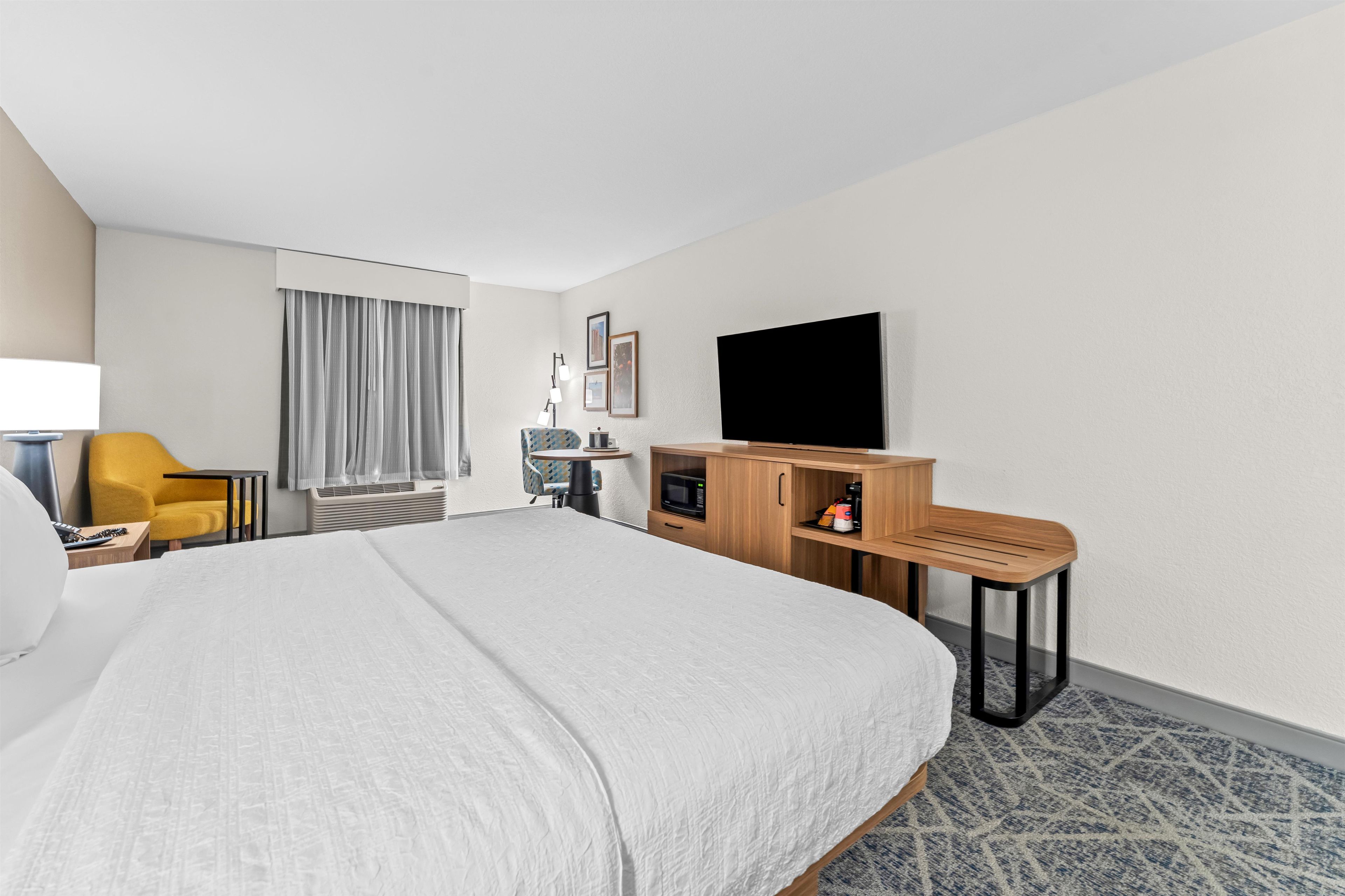 A hotel room with a large bed, a desk, a chair, a flat-screen TV, and a coffee machine.
