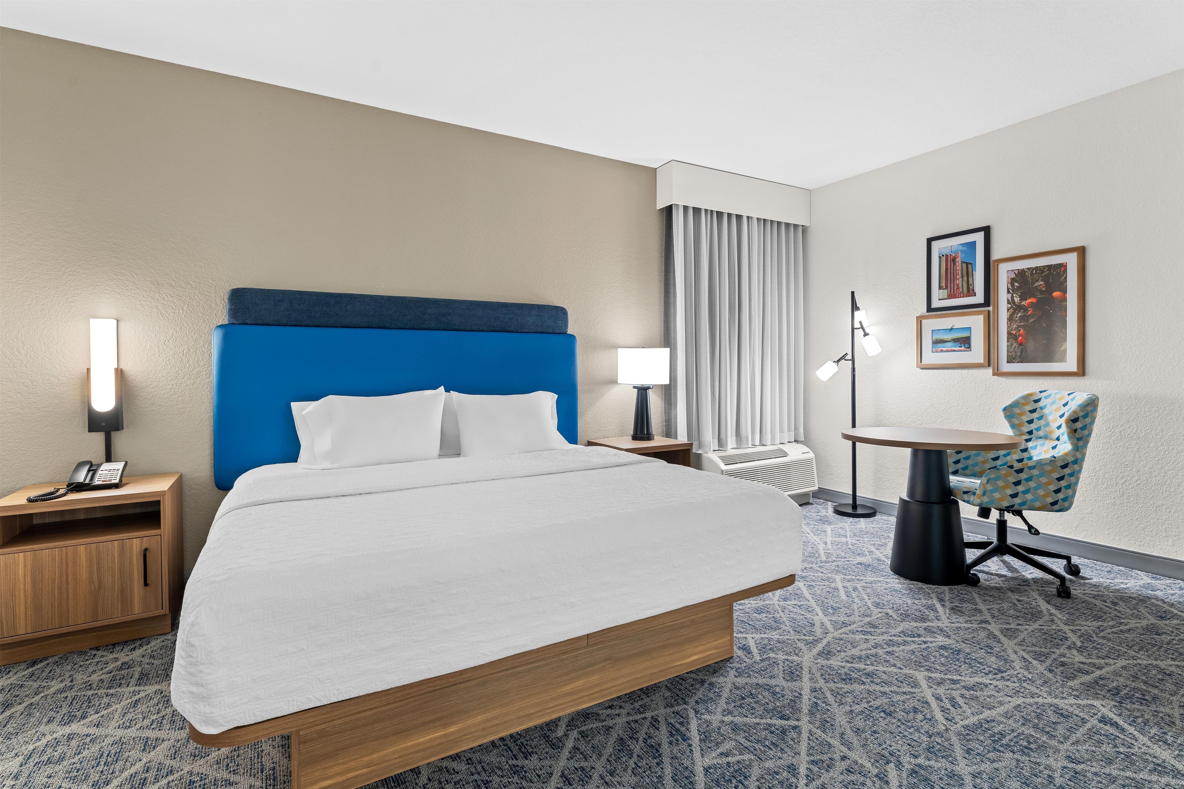 A hotel room with a large bed, a desk, a chair, a lamp, and a picture on the wall.
