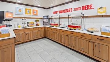 A breakfast area with a counter, coffee machine, and various food items.