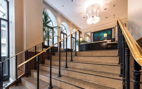 A grand staircase with marble steps and black balusters, leading to a lobby area with a chandelier and large windows.