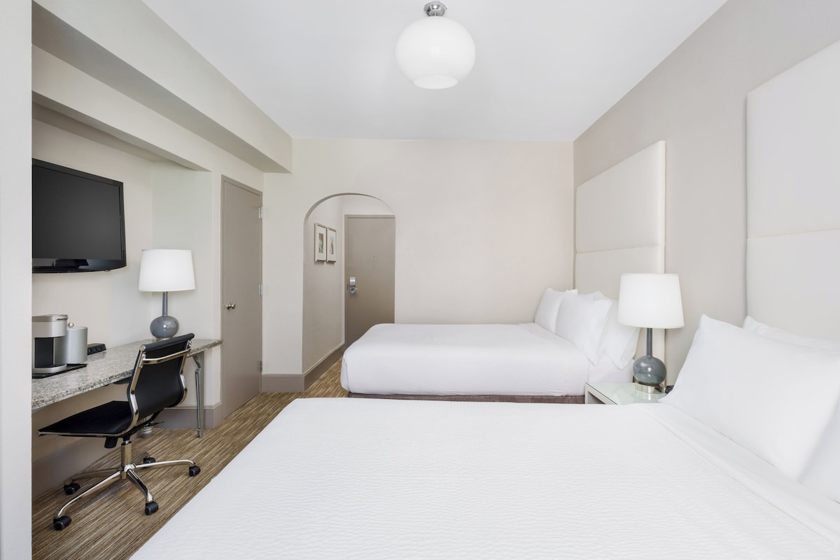 Una camera d'albergo con un letto, una scrivania, una sedia, una TV e una lampada.