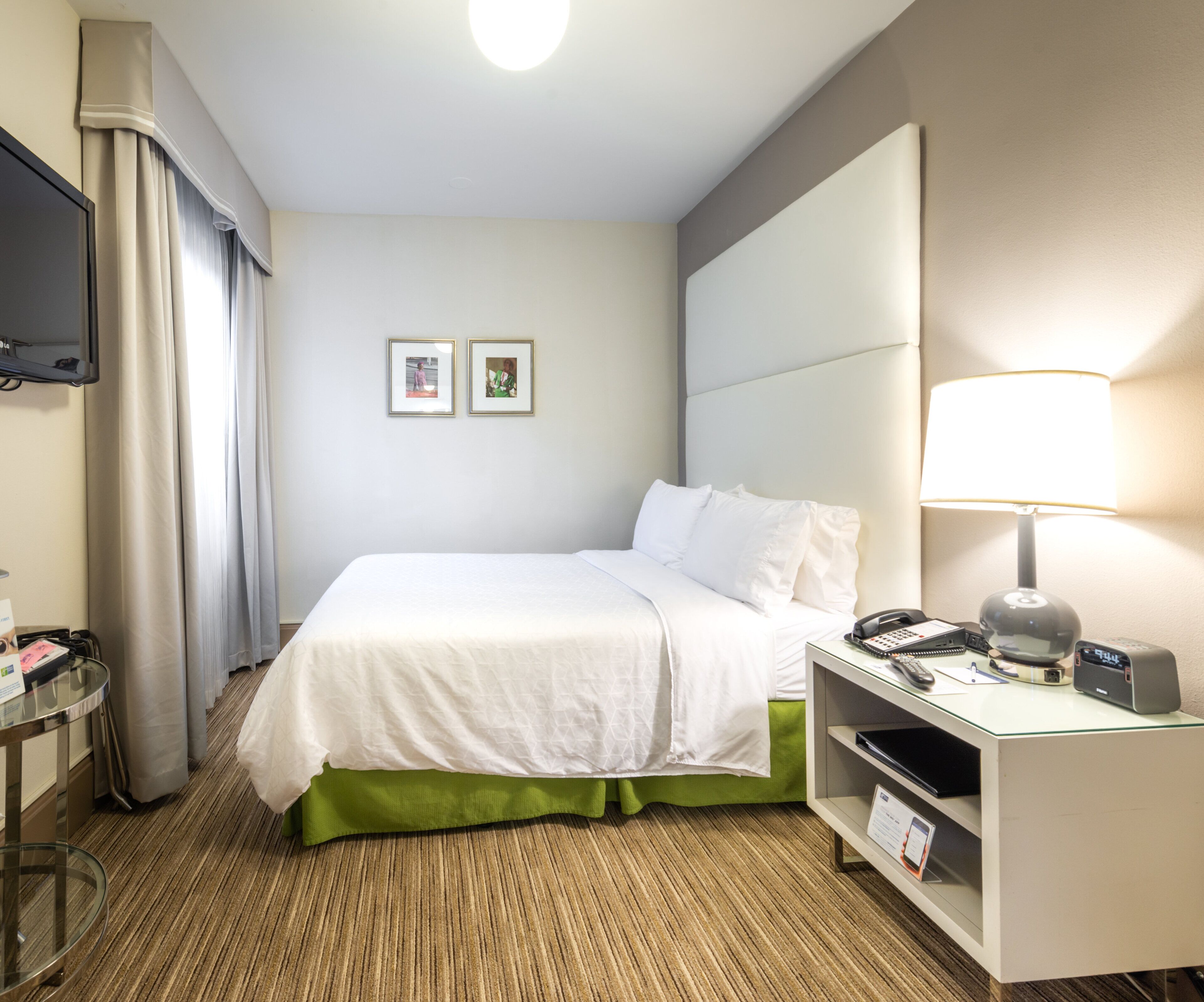 Una camera d'albergo con un letto, una scrivania con una lampada, un telefono e una televisione a parete.