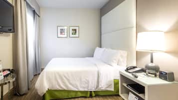 Una camera d'albergo con un letto, una scrivania con una lampada, un telefono e una televisione a parete.