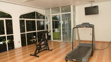 Una habitación amplia con suelo de madera, una bicicleta estática, una cinta de correr y un ventanal con vistas al exterior.
