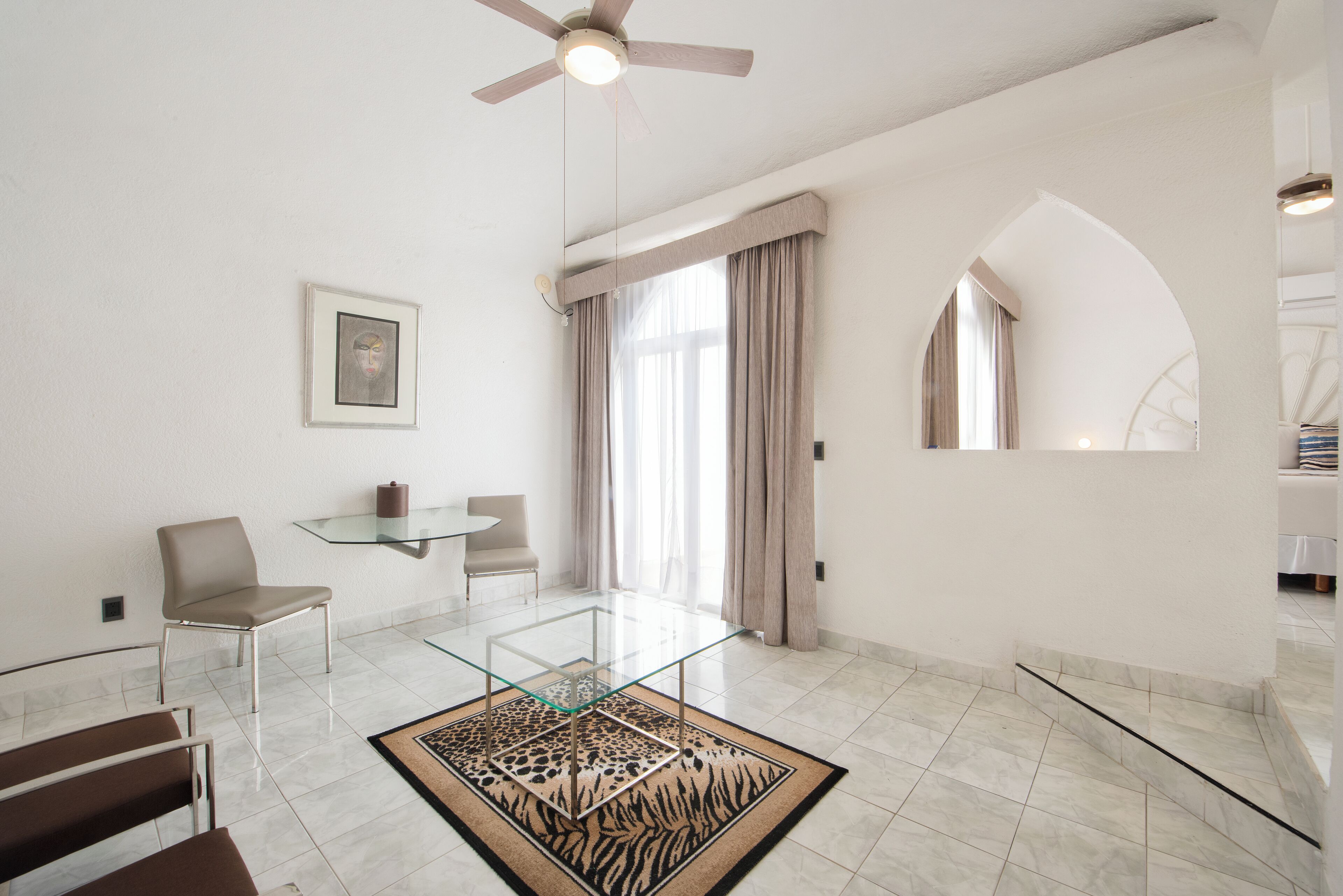 A modern living room with a glass coffee table, a sofa, a chair, and a ceiling fan.
