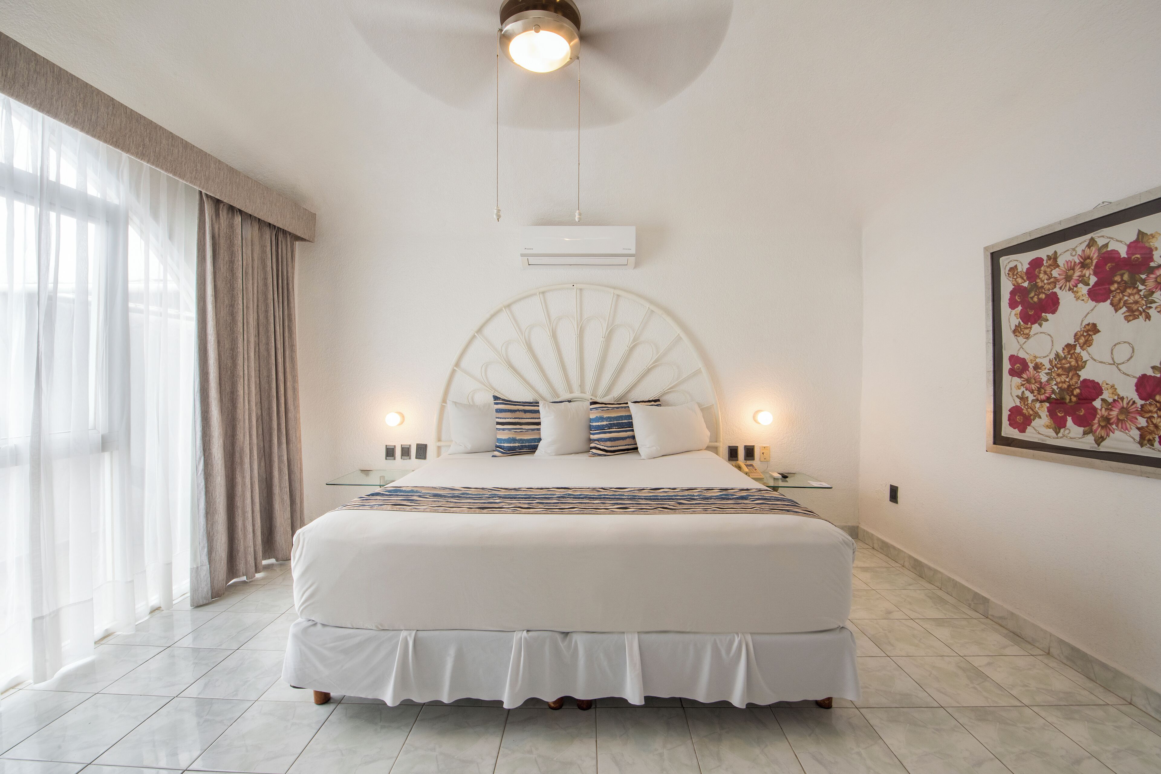 Um quarto espaçoso com uma cama grande, um ventilador de teto e um ar condicionado fixado na parede.