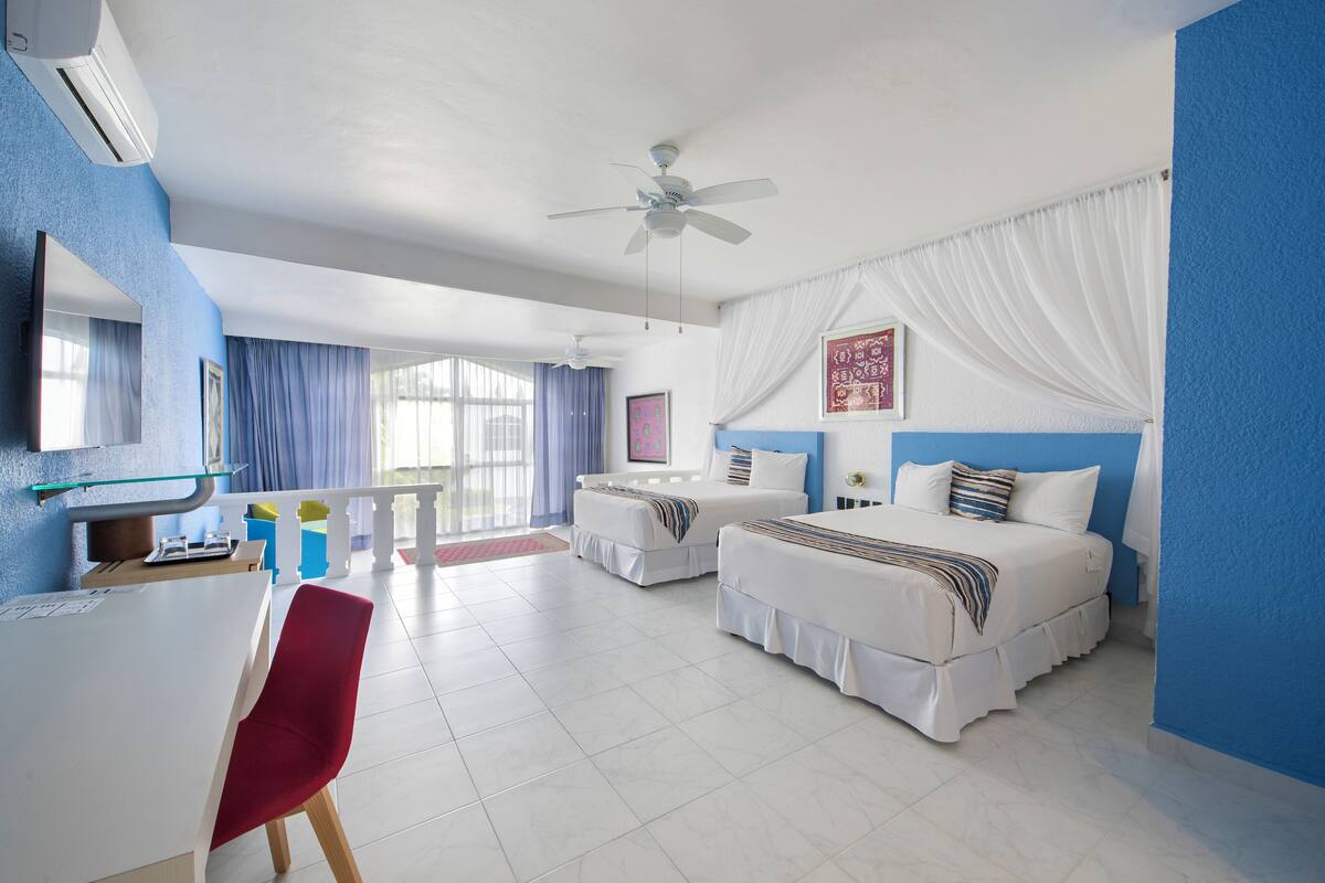 A hotel room with two beds, a desk, a chair, and a ceiling fan.