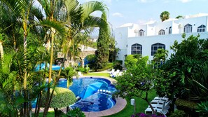 Una piscina rodeada de exuberante follaje y un edificio blanco con ventanas de arco.