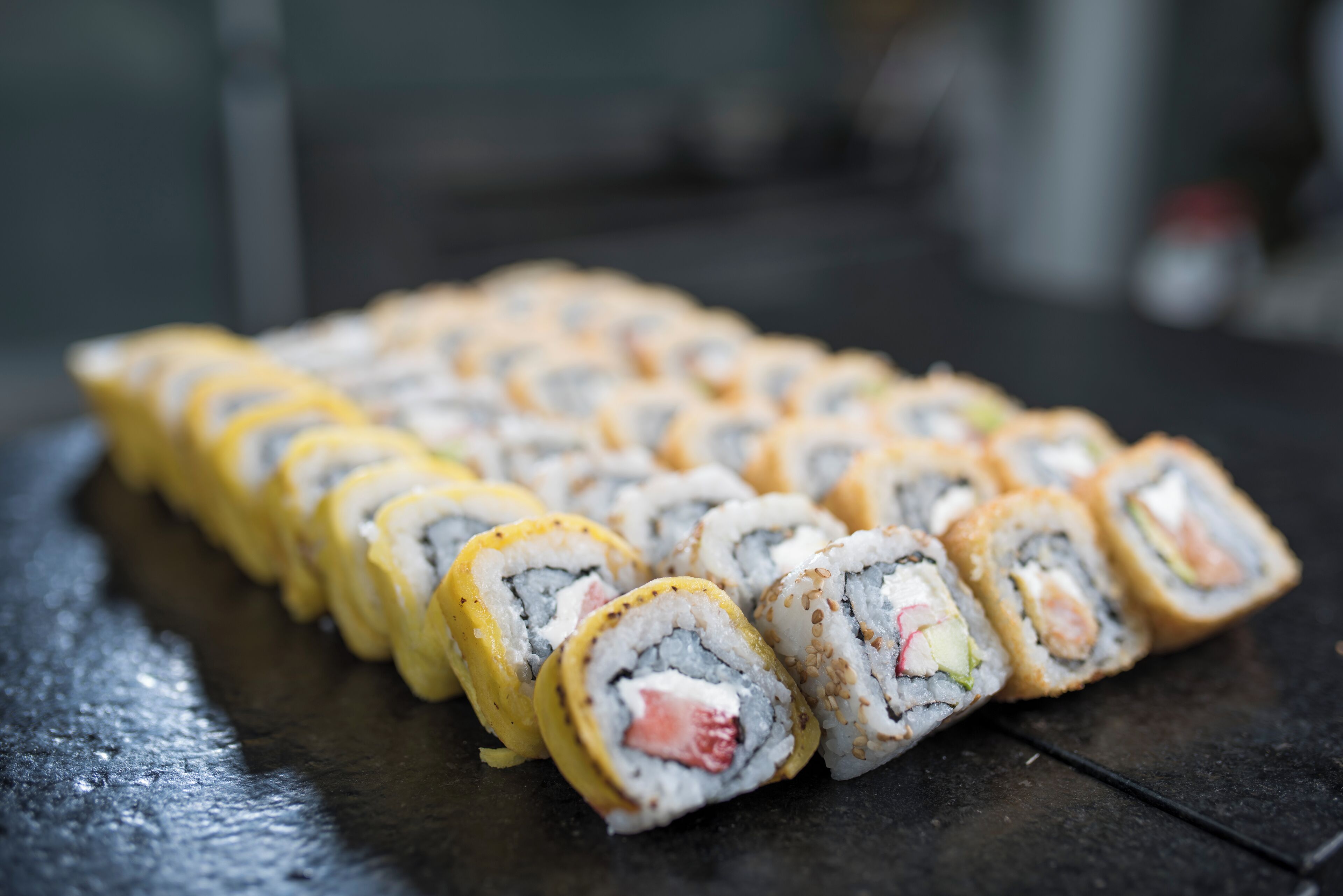 Un plato de sushi ordenado con diversos rellenos sobre una superficie oscura.
