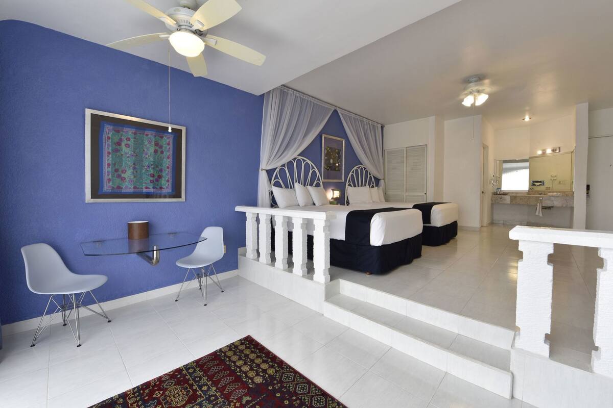 A room with a bed, a white bench, a glass table, and chairs.