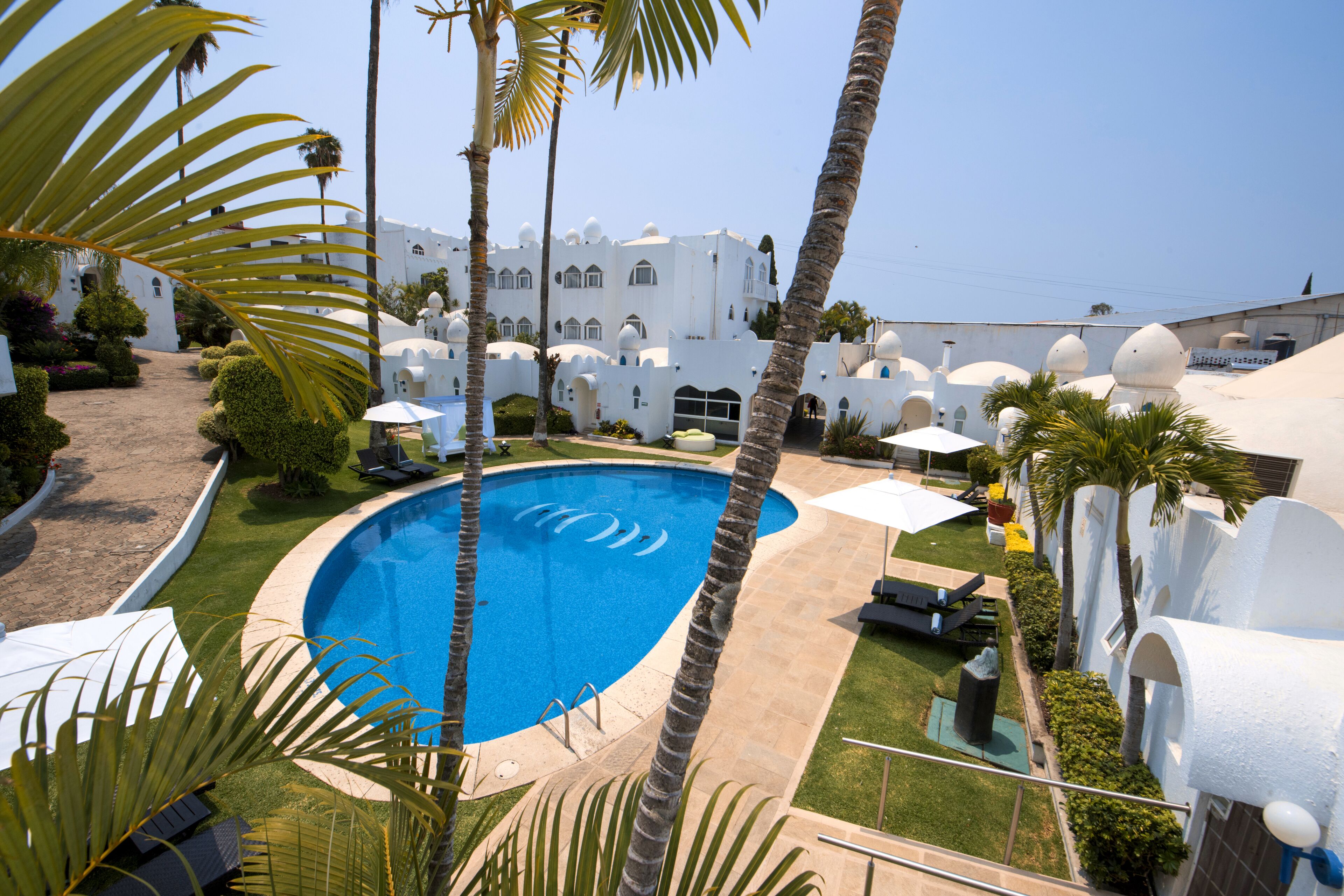 Una piscina rodeada de palmeras y un edificio blanco con techo abovedado.