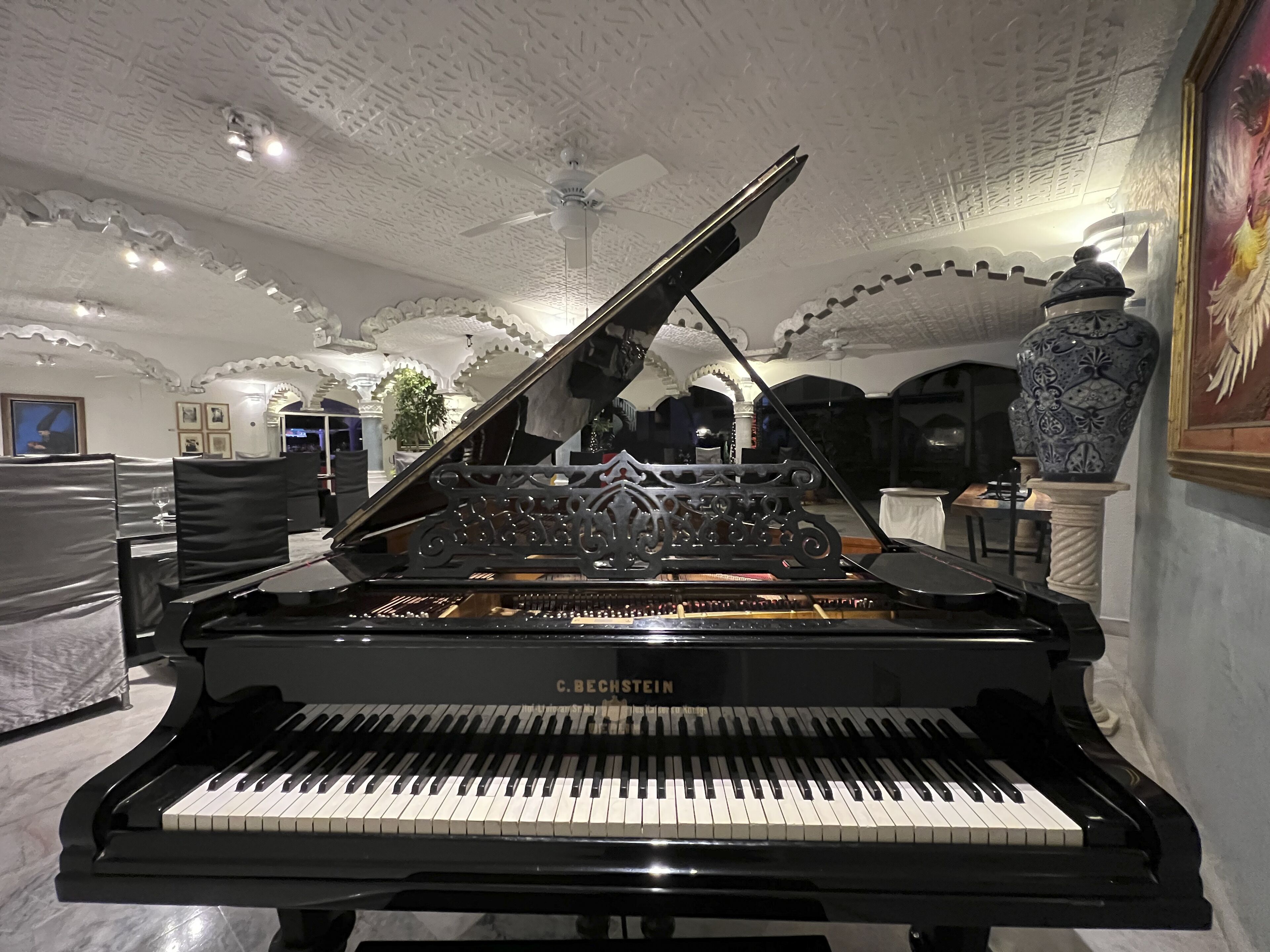 Un piano de cola en una habitación amplia con detalles ornamentales en el techo y las paredes.