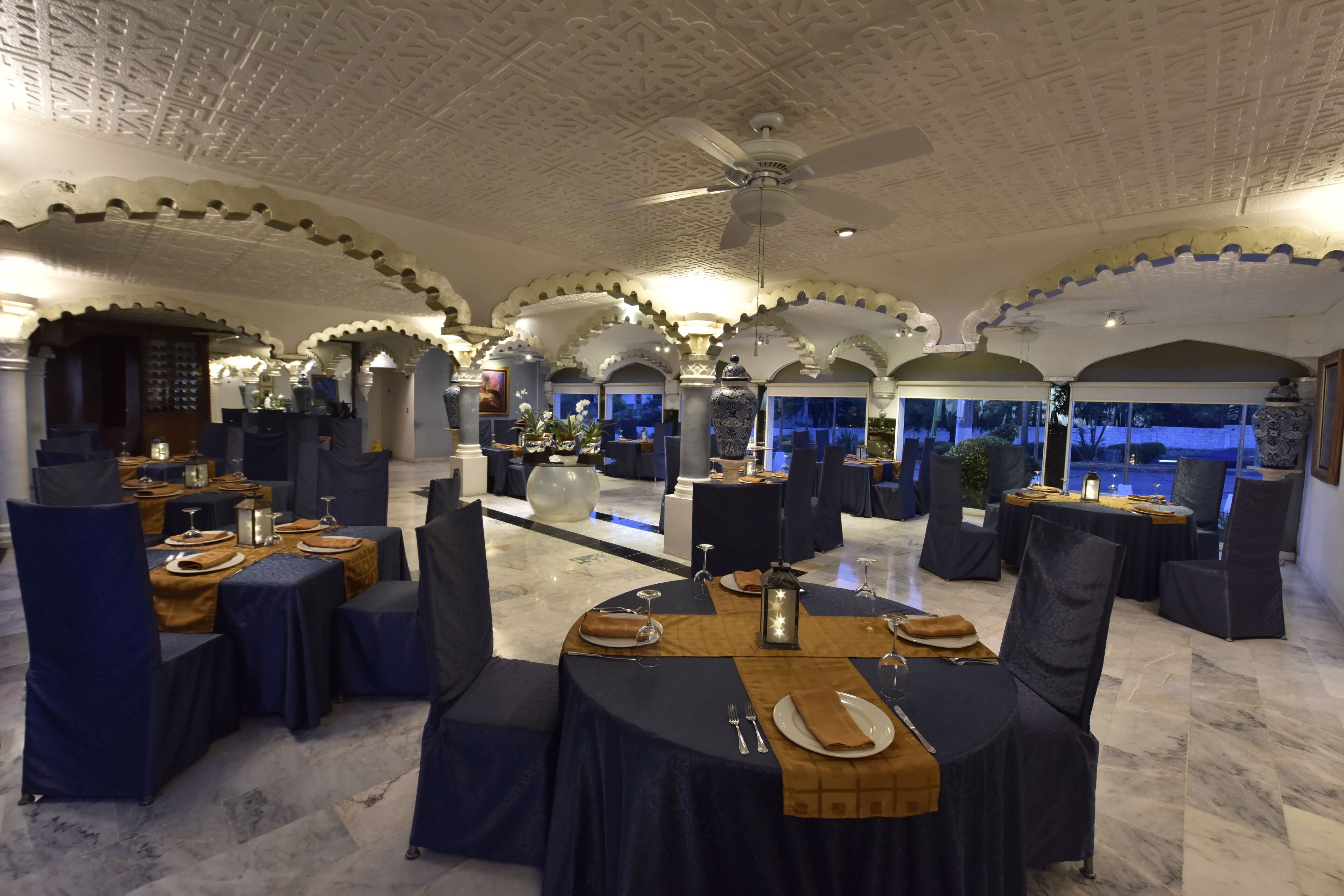 A restaurant with round tables, dark blue tablecloths, and a ceiling fan.